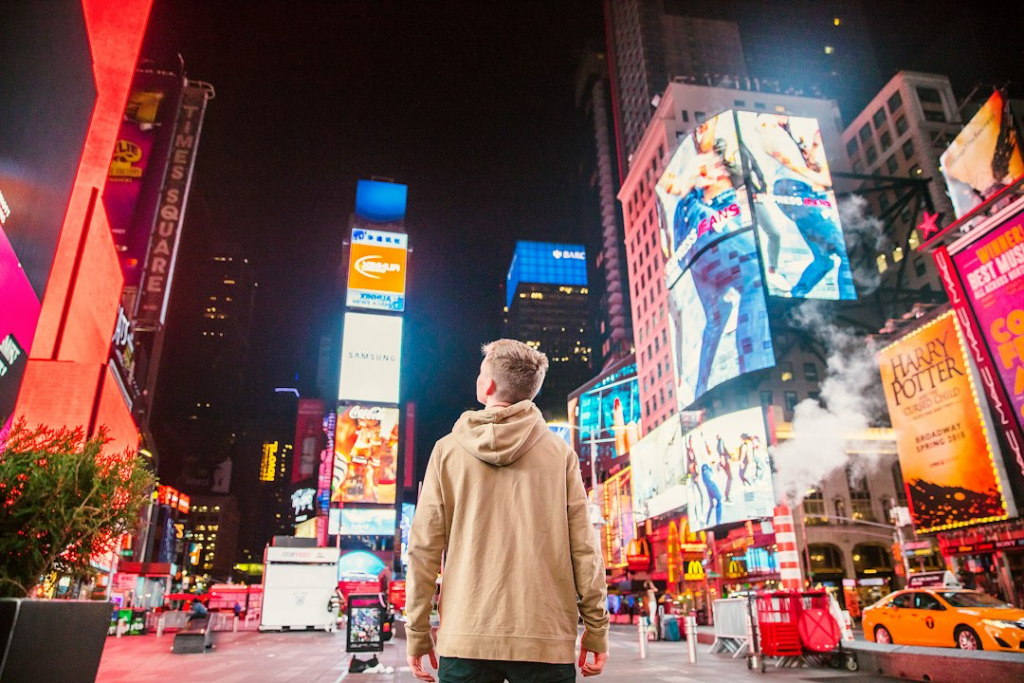 Man standing staring at digital bill boards and advertising in a busy street.